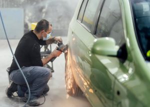 A mechanic working on the body of a car in an auto repair shop, symbolizing the process of collision repair after an accident.