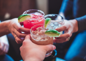A group of people cheering with alcoholic drinks at a restaurant, symbolizing a social occasion where alcohol laws apply.