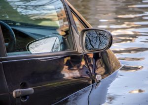 A car almost completely submerged in muddy floodwater, symbolizing a natural disaster and its potential impact on auto insurance claims.