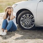 worried woman sitting next to car