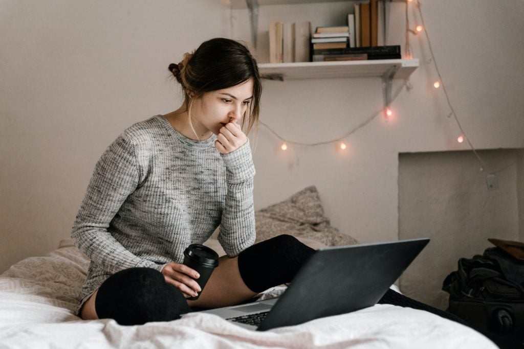 woman with take-out coffee cup reading laptop computer