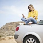 woman sitting on car with smartphone
