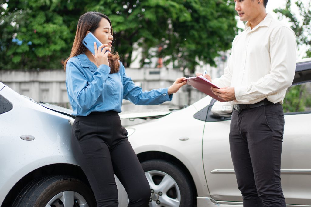 women driver Talk to Insurance Agent for examining damaged car and customer checking on report claim form after an accident. Concept of insurance and car traffic accidents