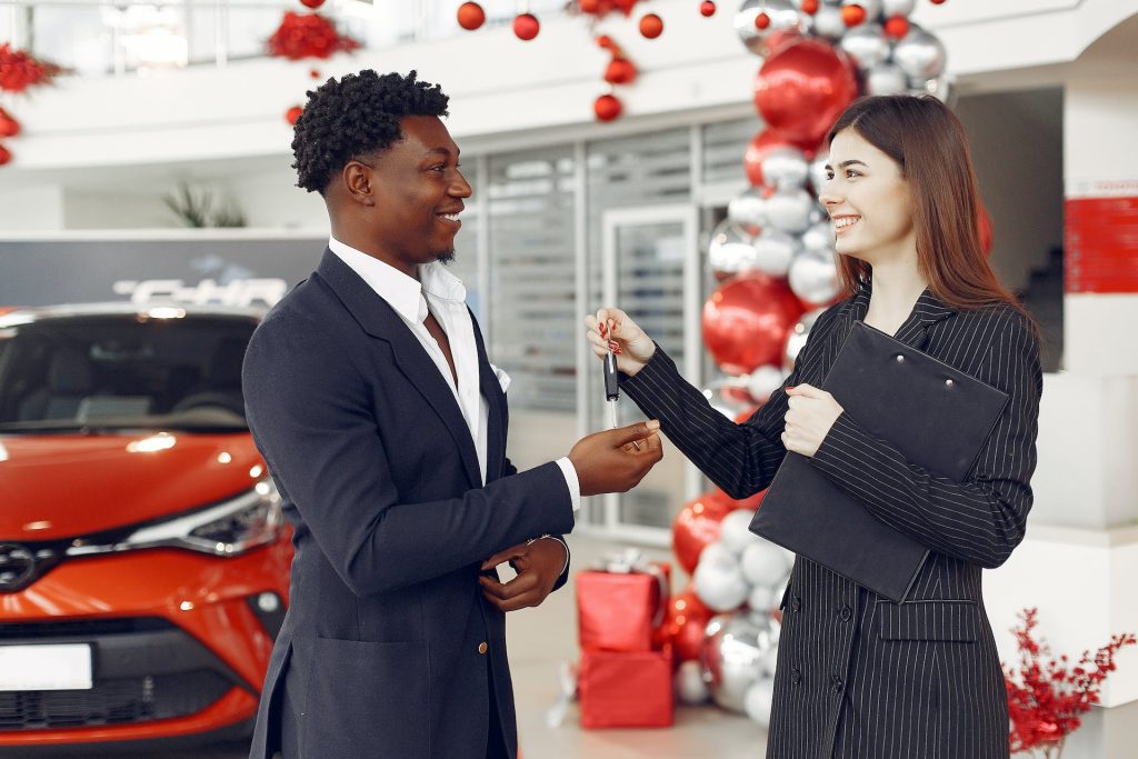 man getting keys to new car from sales woman at dealership