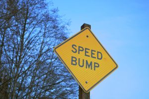 A yellow road sign with the classic bumpy symbol for "speed bump ahead," symbolizing a traditional method for traffic calming.