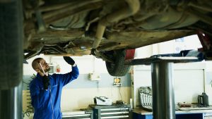 A mechanic working underneath a car, symbolizing the installation of a catalytic converter anti-theft device.