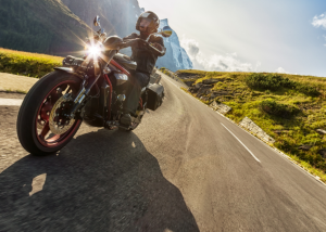 A man wearing a helmet and leather jacket riding a motorcycle down a scenic road, symbolizingstates with the most motorcycles .