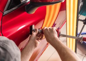 A man using specialized tools to remove a small dent from a car, symbolizing the paintless dent removal (PDR) process.